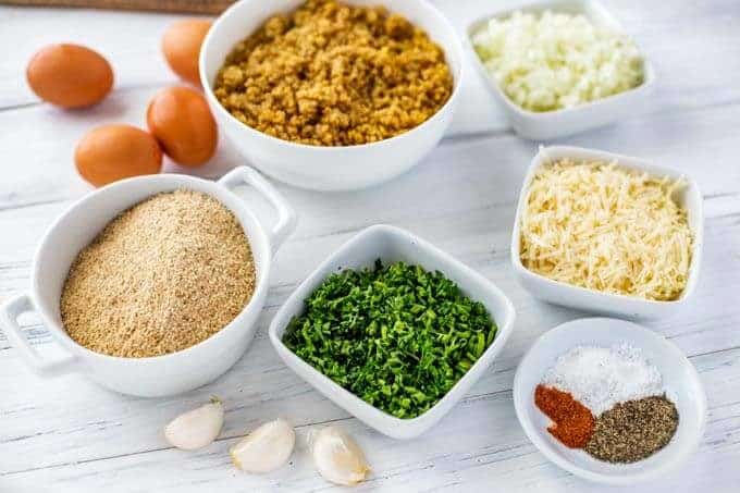 Photo of Ingredients in small white bowls: Quinoa, eggs, onion, gluten free breadcrumbs, garlic, parsley, seasonings and parmesan.