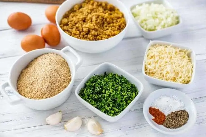 Photo of Ingredients in small white bowls: Quinoa, eggs, onion, gluten free breadcrumbs, garlic, parsley, seasonings and parmesan.