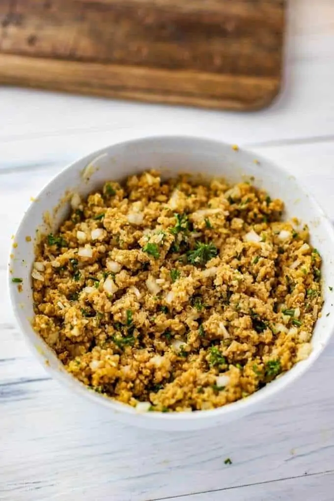 Photo of cooked quinoa, eggs, cayenne pepper, salt, black pepper, chives, Parmesan, garlic, and gluten free breadcrumbs in a white bowl.