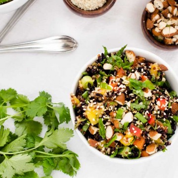 Overhead photo of a bowl of Thai Quinoa Salad surrounded by cilantro, sesame seeds, and almonds.