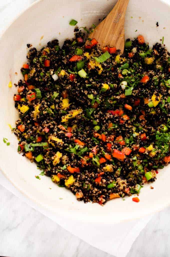 Photo of cooked quinoa, cooked, black rice, mango, red pepper, green onions, cilantro, and mint tossed with dressing in a large white bowl with a spoon in it.