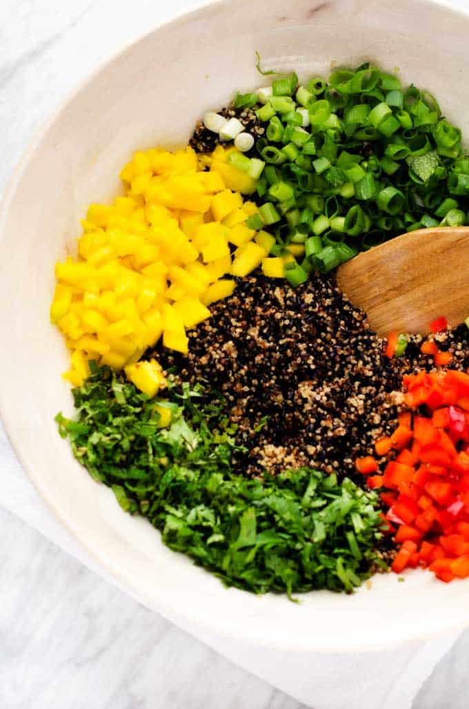 Photo of cooked quinoa, cooked, black rice, mango, red pepper, green onions, cilantro, and mint in a large white bowl.