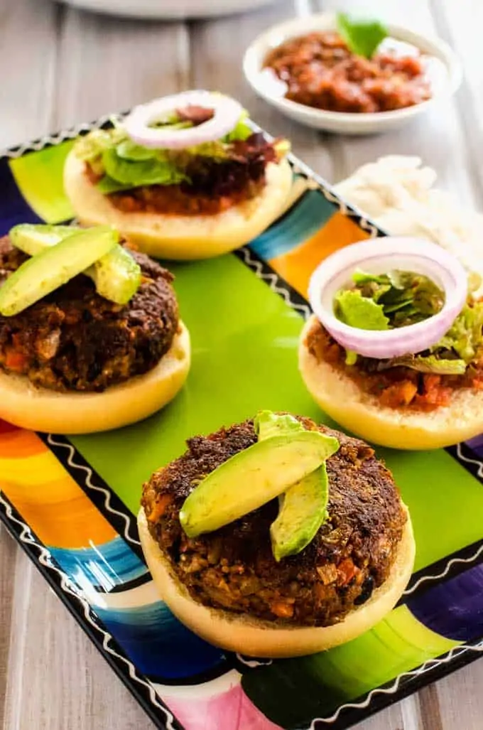 Photo of two Quinoa Burgers on buns garnished with avocado sitting on a colorful plate.