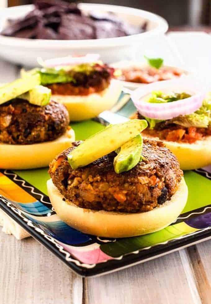 Close up photo of Quinoa Burgers garnished with avocado sitting on a colorful fiesta inspired plate.