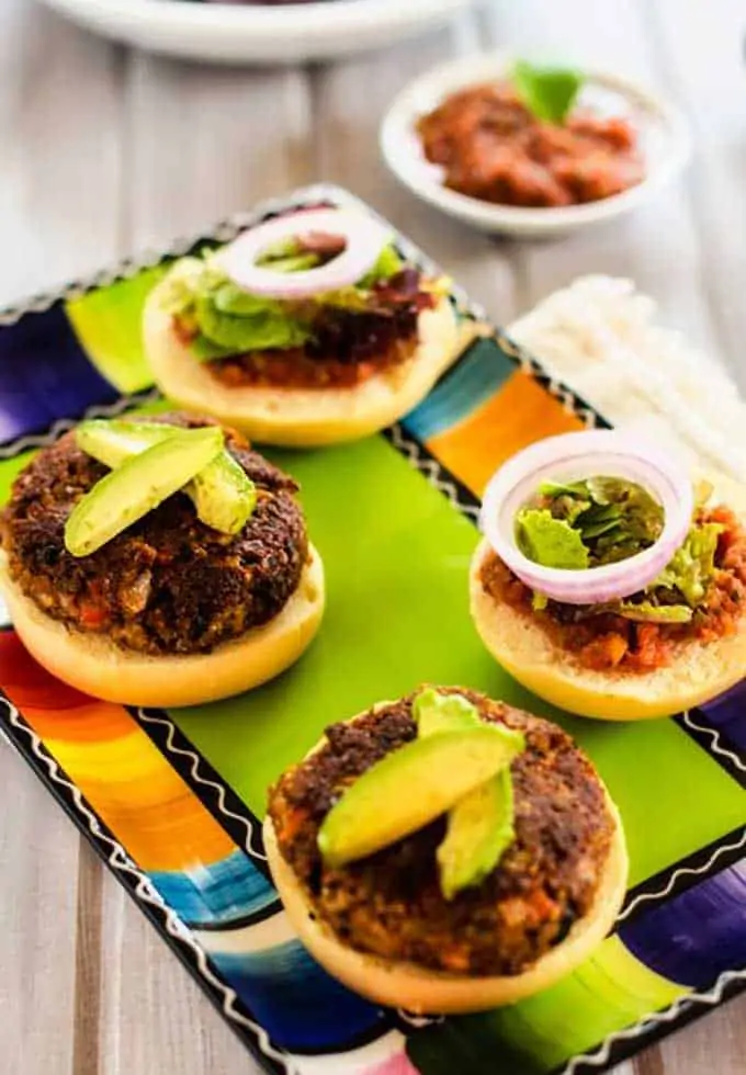 Photo of two Mexican Quinoa Burgers sitting on a colorful plate garnished with avocado with a small dish of salsa behind them.