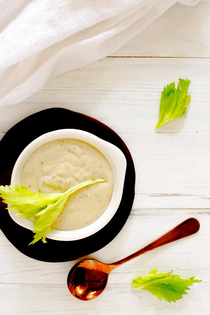 Overhead photo of Cream of Celery Soup in a white bowl garnished with celery leaves sitting on a small wooden plate.