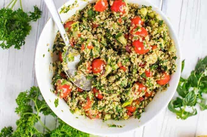 A large white bowl with quinoa tabbouleh being mixed up in it.
