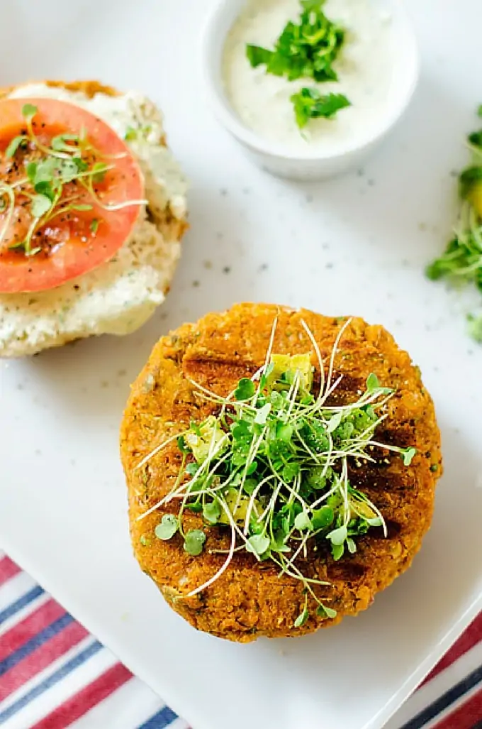 Overhead photo of a Sweet Potato Burger on a bun garnished with microgreens with the other half of the bun sitting next to it with a tomato and microgreens.