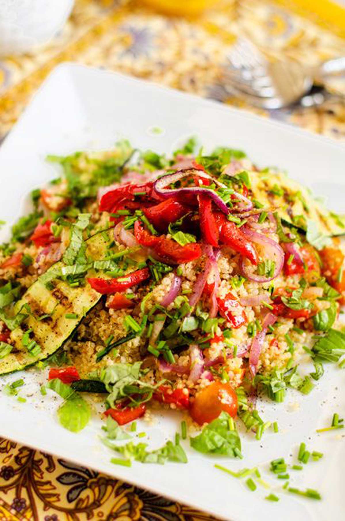 Photo of a white square plate with a vegetable quinoa salad garnished with fresh herbs.