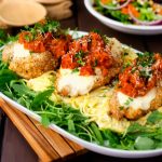 Square photo of healthy chicken parmesan on a bed of pasta surrounded by spinach.