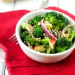 Photo of a white bowl with broccoli apple salad sitting on a red napkin.