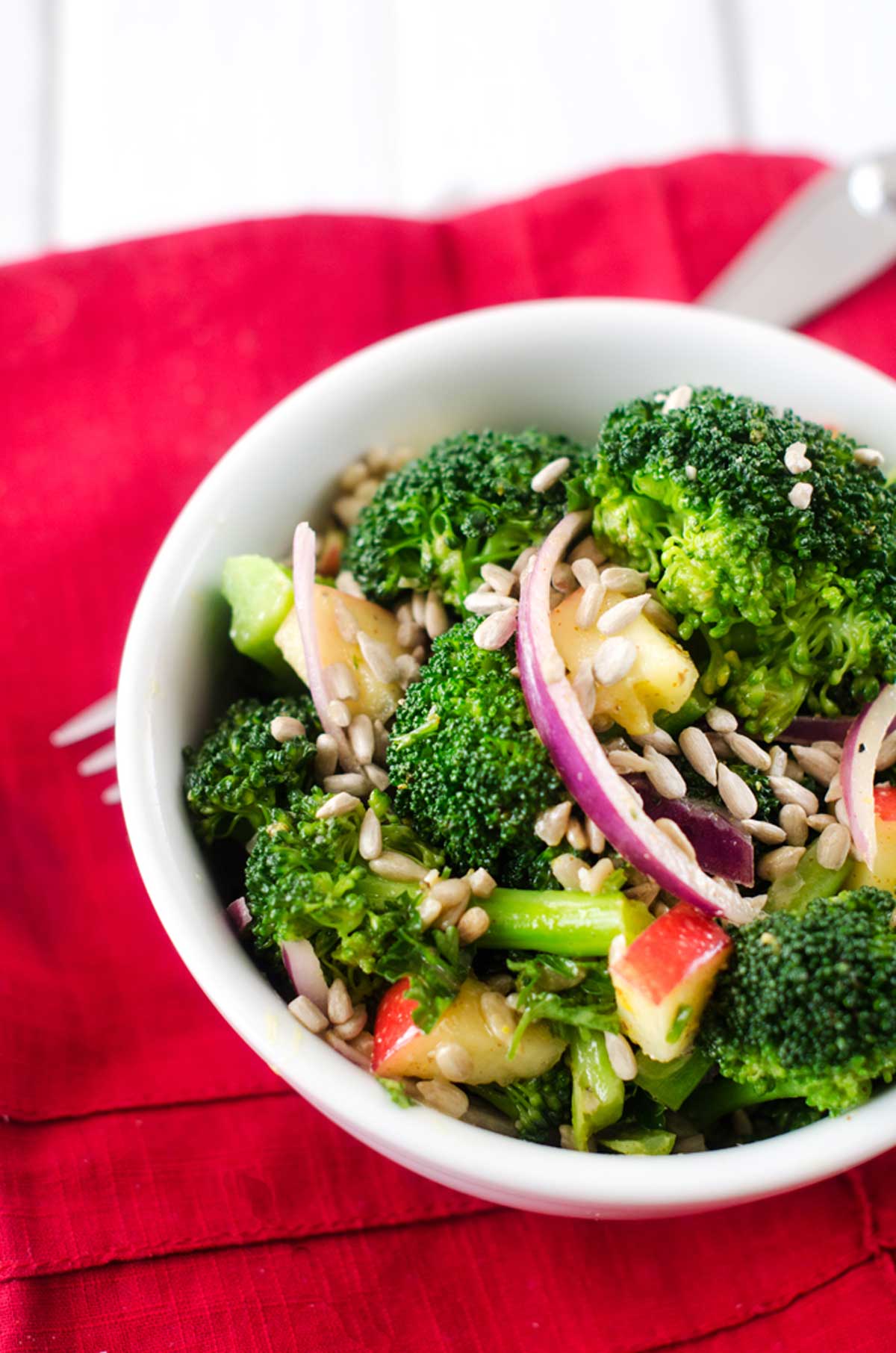 Photo of a white bowl of apple broccoli salad sitting on a red napkin.