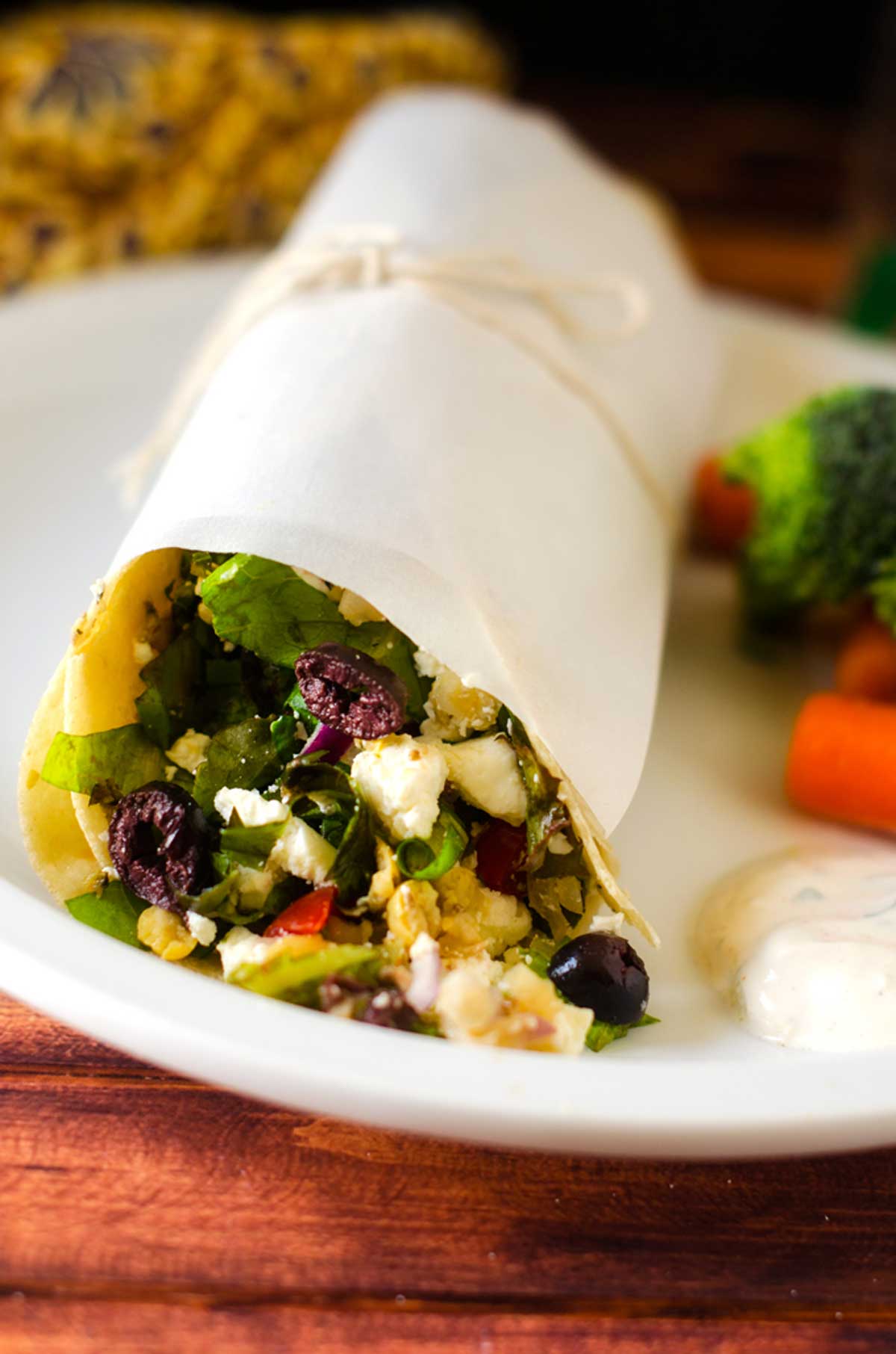 Side photo of a greek salad wrap on a white plate.