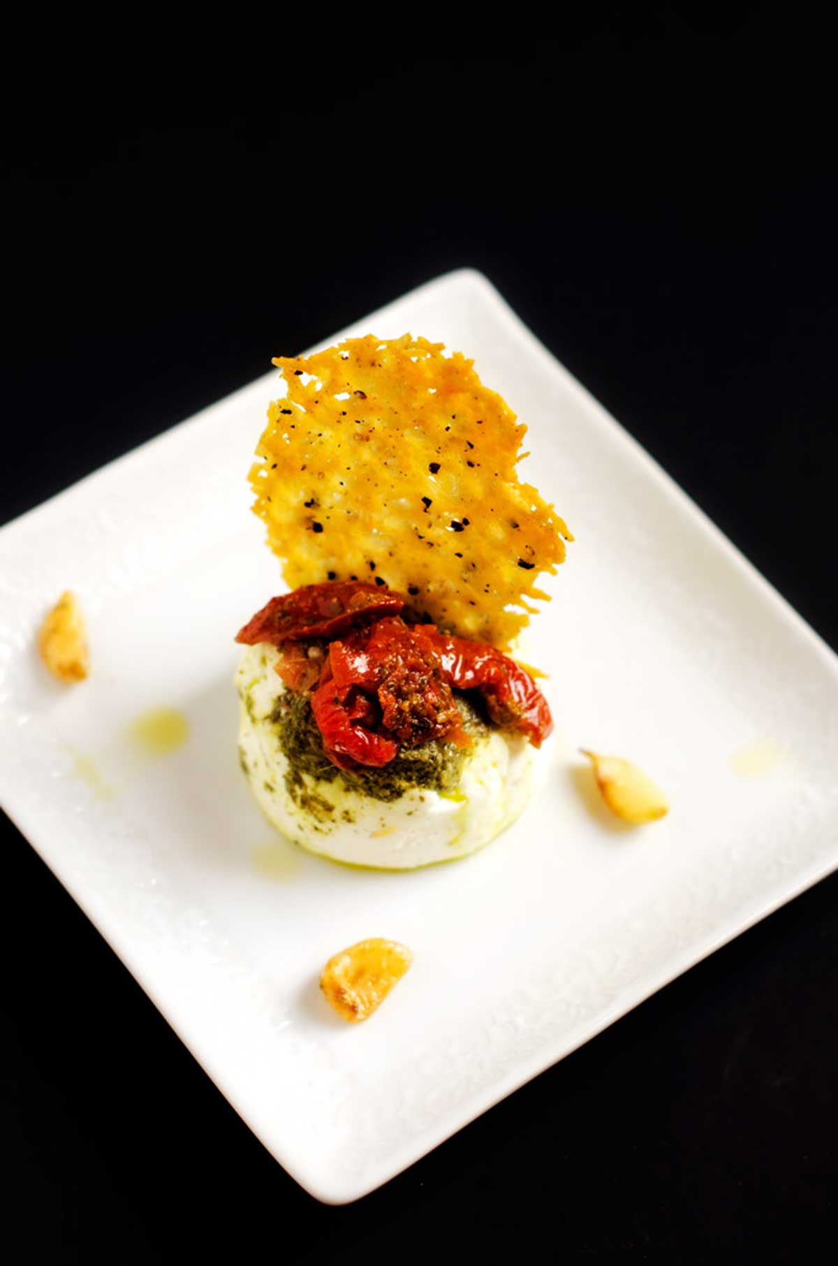 Photo of a white plate on a black background with a parmesan crisp sticking out of a cheese round.