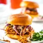 Side photo of two Slow Cooker BBQ Chicken Sandwiches on white plates.