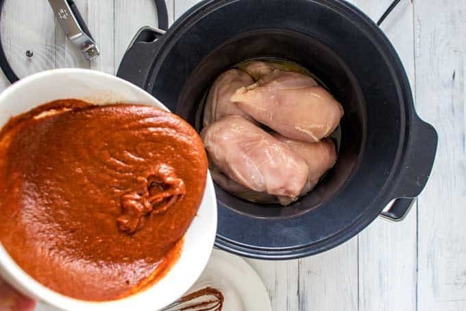 Photo of BBQ sauce being poured over chicken in a slow cooker.