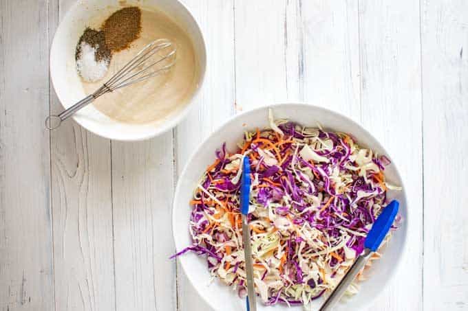 Photo of a bowl of cabbage and carrots with a slaw dressing sitting next to it.