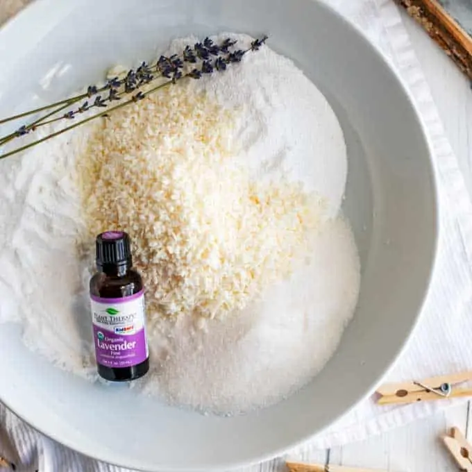 Photo of the ingredients for DIY Laundry Detergent in a large white bowl with lavender essential oil.