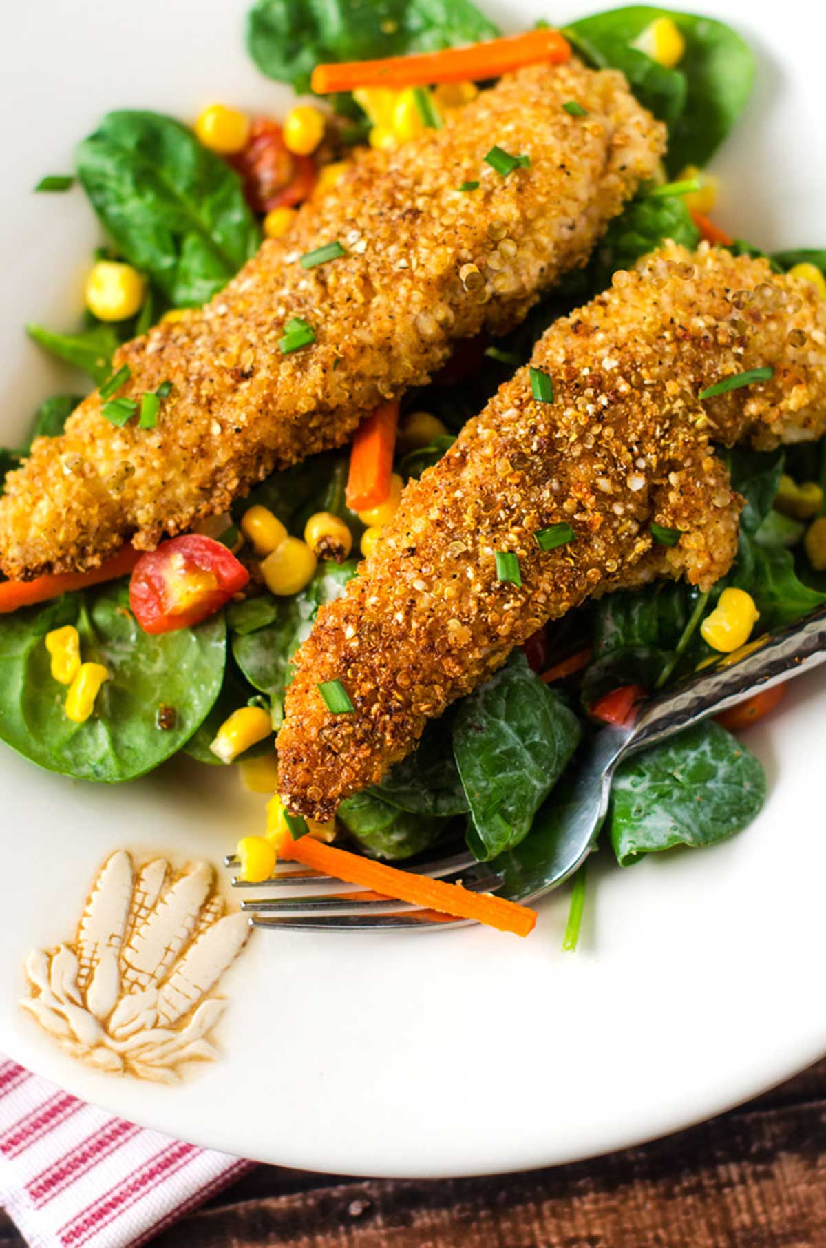 Close up photo of quinoa crusted chicken on a green salad.