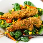 Square photo of crispy quinoa crusted chicken served on top of a vibrant salad.
