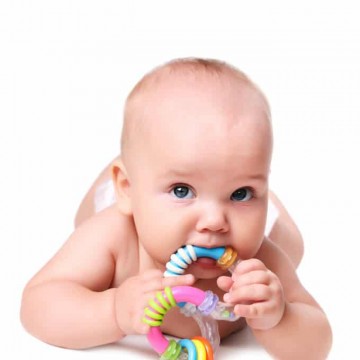 Photo of a baby with a teething ring laying on his stomach on a white background.