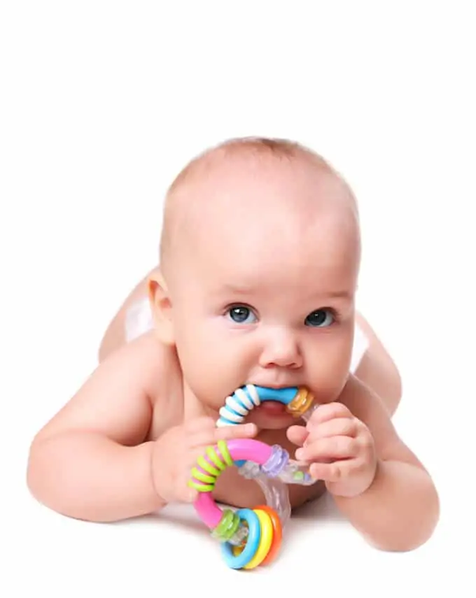 Photo of a baby with a teething ring laying on his stomach on a white background.