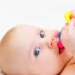 Photo of a baby with a teething ring laying on his back against a white background - Essential Oils for Teething.