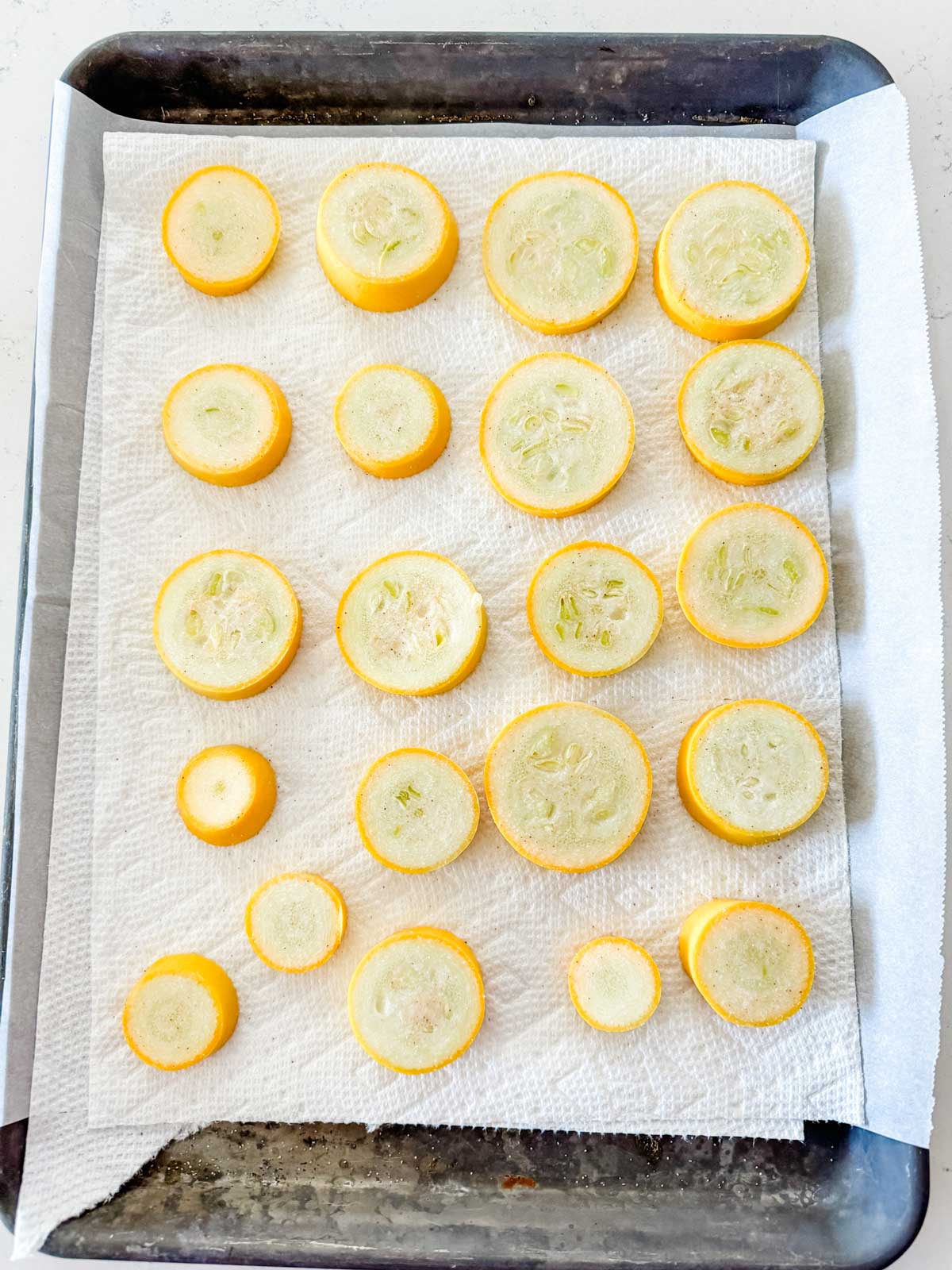 Photo of sliced summer squash on a paper towel lined baking sheet.