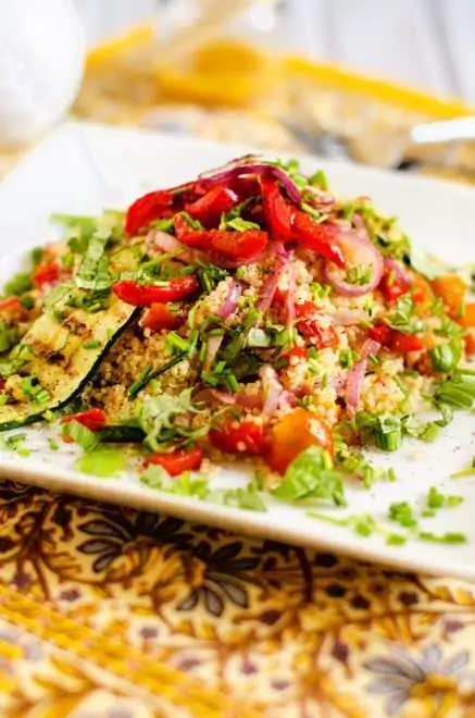 Side photo of a grilled vegetable quinoa salad on a white plate garnished with herbs.