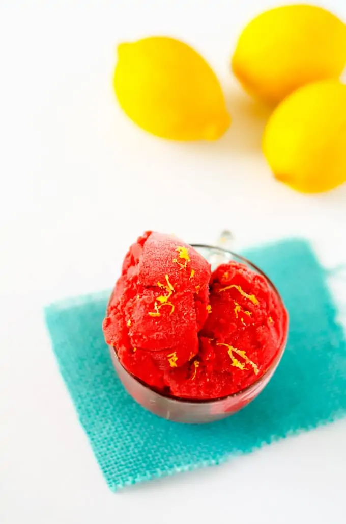 Photo of a glass dish with strawberry sorbet sitting in front of a bunch of fresh lemons.