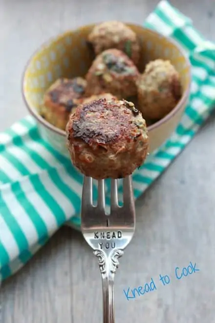 Photo of a bowl of Turkey Quinoa Meatballs on a green and white napkin with a fork in front of it with a single meatball.