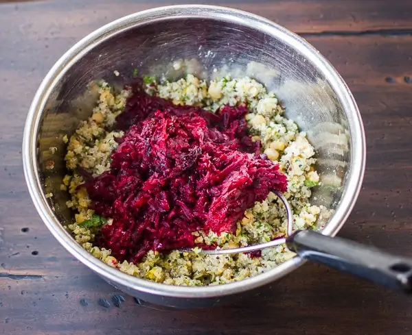 Photo of the ingredients for a Beet Burger with quinoa and chickpeas being mixed together in a metal bowl.