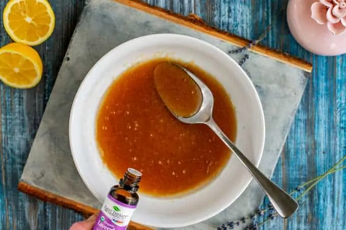 Photo of lavender essential oil being added to a bowl with raw sugar, avocado oil, and lemon juice.
