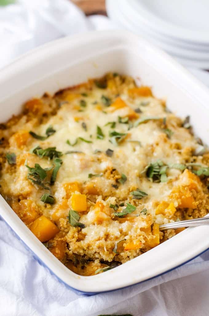 Photo of Butternut Squash Casserole with Quinoa in a casserole dish garnished with sage against a white background.