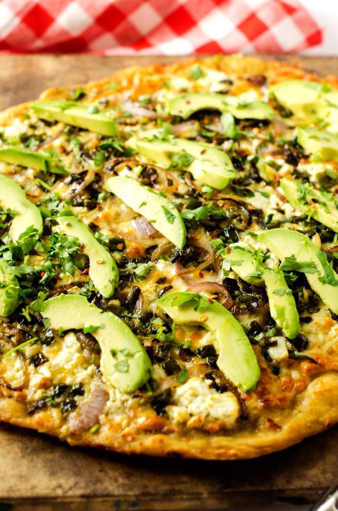 Photo of a whole Avocado Pizza with PepperJack and Poblano Peppers on a pizza stone with a red and white checkered napkin behind it.