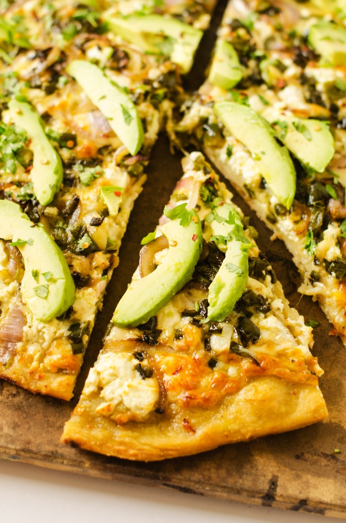 Photo of a Avocado Pizza with PepperJack and Poblano Peppers on a pizza stone with a pizza slice cut out.