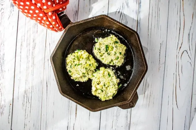Photo of Zucchini Fritters being cooked in a cast iron skillet.