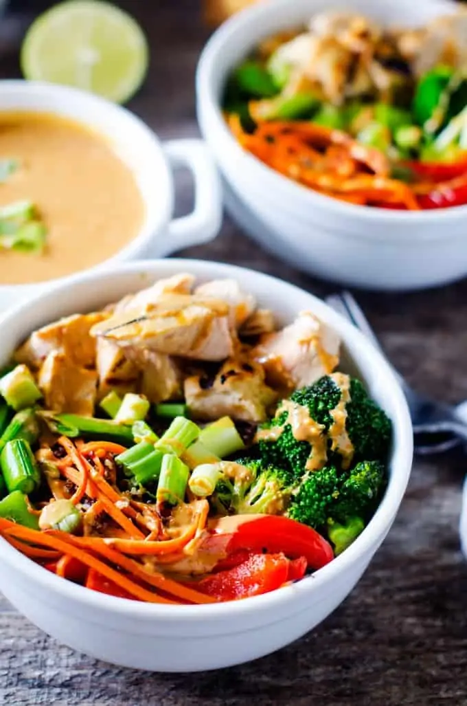Photo of a prepared Veggie Quinoa Bowl recipe divided among two white bowls with a small dish of a Spicy Peanut Sauce.