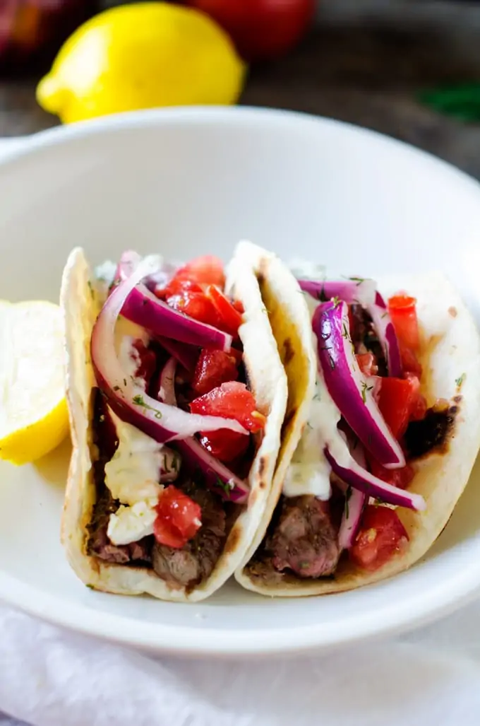 Side photo of a prepared Steak Gyro Recipe on a white plate with a lemon garnish.