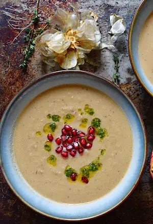 Photo of Creamy Roasted Garlic and Cauliflower Soup in a blue bowl garnished with pomegranates.