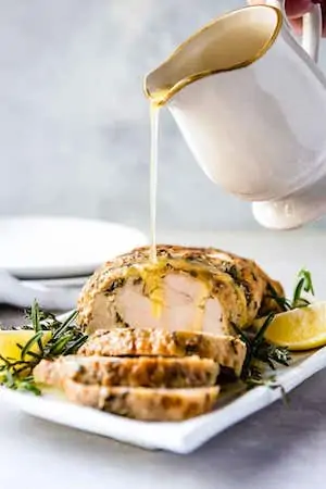 Photo of Instant Pot Turkey Breast on a white serving platter with gravy being poured over it.