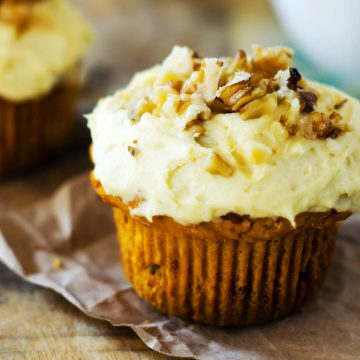 Square side photo of a gluten free pumpkin muffin with cream cheese frosting topped with walnuts.