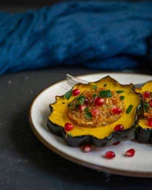 Photo of Quinoa Stuffed Acorn Squash Rings on a white plate sitting on a black surface.