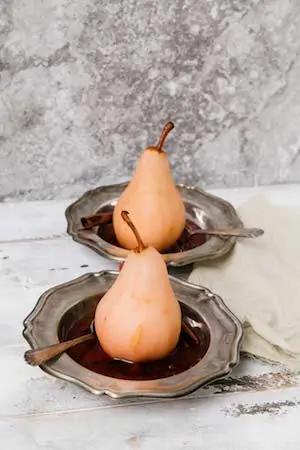 Photo of two cranberry poached pears on silver platters against a light grey background.