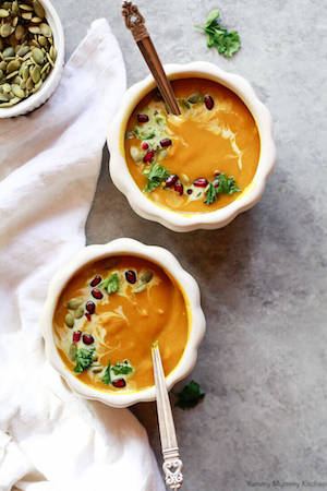 Overhead photo of two bowls of curried butternut squash pumpkin soup on a light gray background.