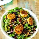 Overhead photo of a fried goat cheese salad on a white bowl against a rustic wooden background.