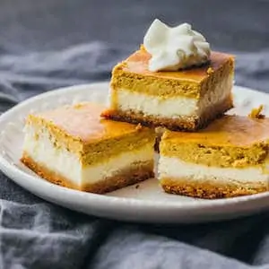 Photo of three Pumpkin Cheesecake Bars stacked on a white plate.