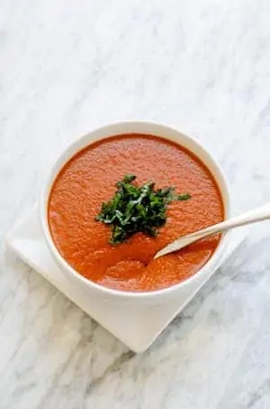 Overhead photo of Roasted Red Pepper Tomato Soup in a white bowl against a white background.