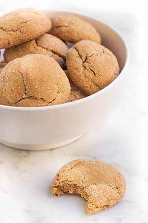 Photo of ginger cookies in a white bowl with one cookie sitting beside the bowl.