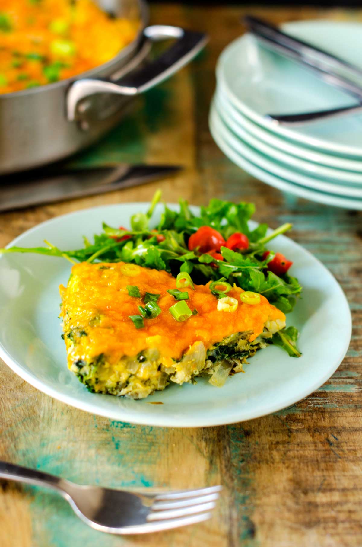 Photo of a light blue plate with a spinach artichoke frittata sitting next to a green salad.